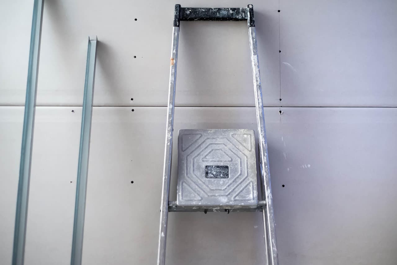 Sheets of plasterboard fixed to a wall, with a stepladder and a tray of tools