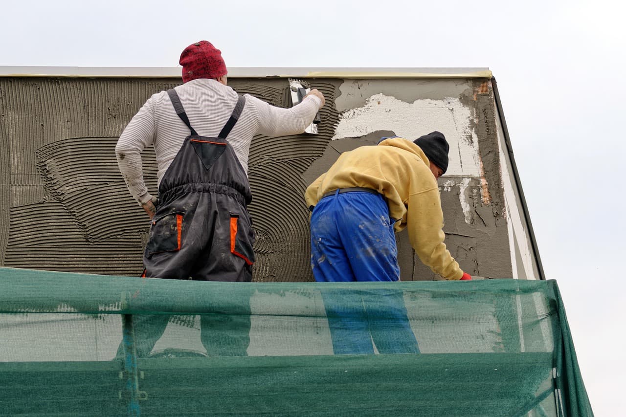 Two plasterers rendering the outside wall of a house from a scaffold